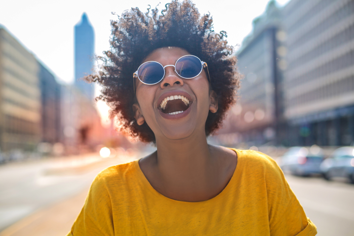 Brown woman smiling, outside in the city on a sunny day